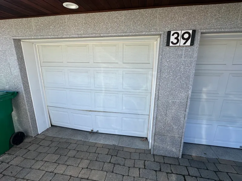 Damaged and misaligned white garage door panel needing replacement